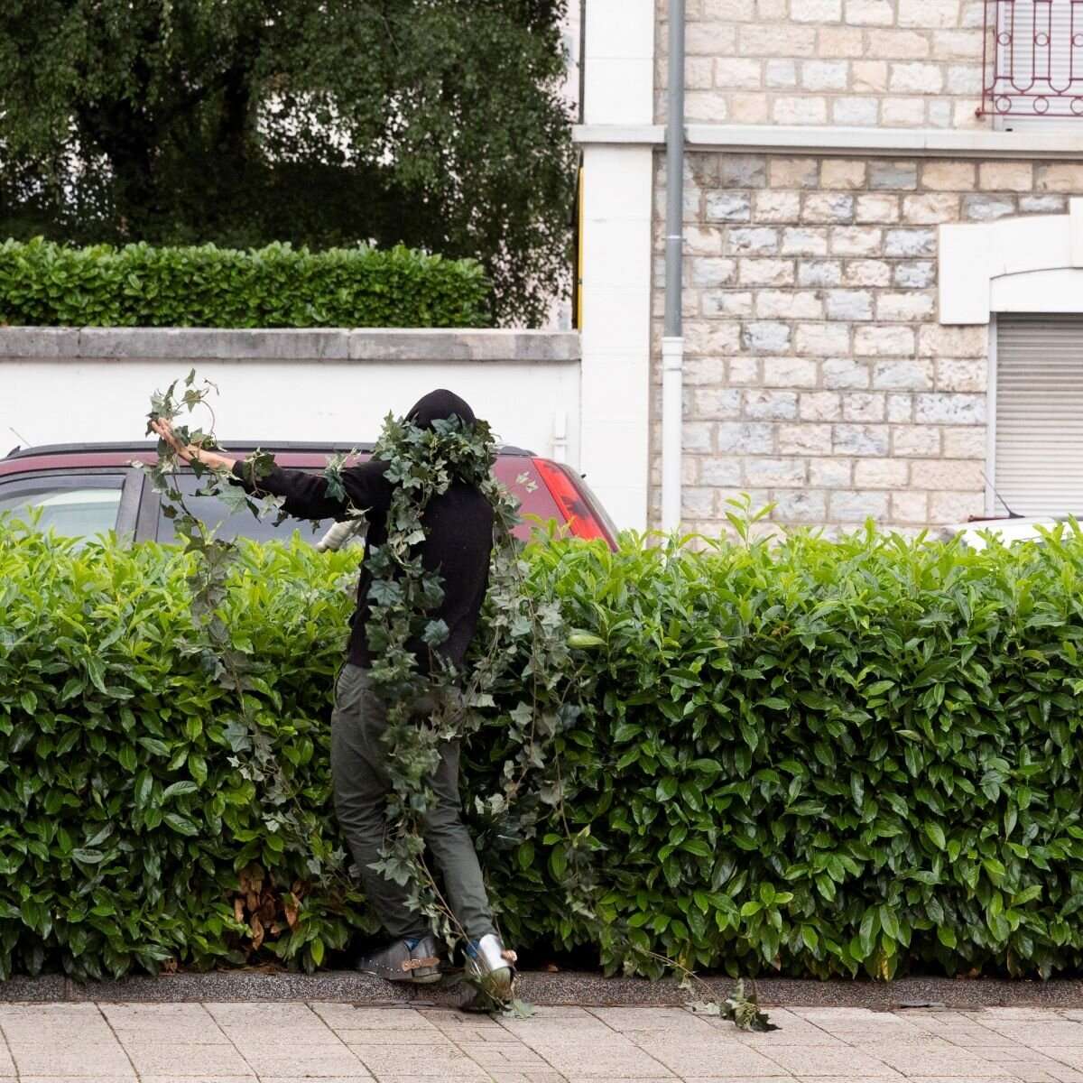 Un homme camouflé devant une haie