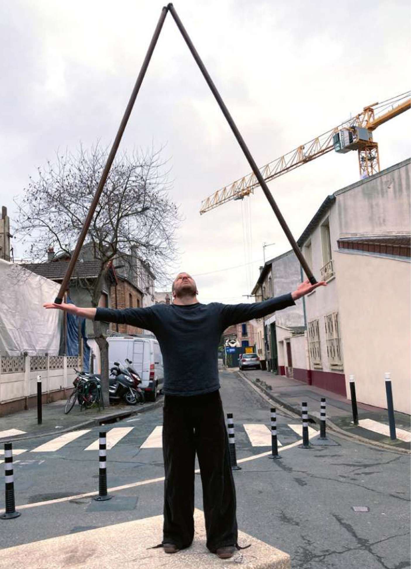 Un homme dans la rue tient 2 bâtons en équilibre sur ses paumes de main