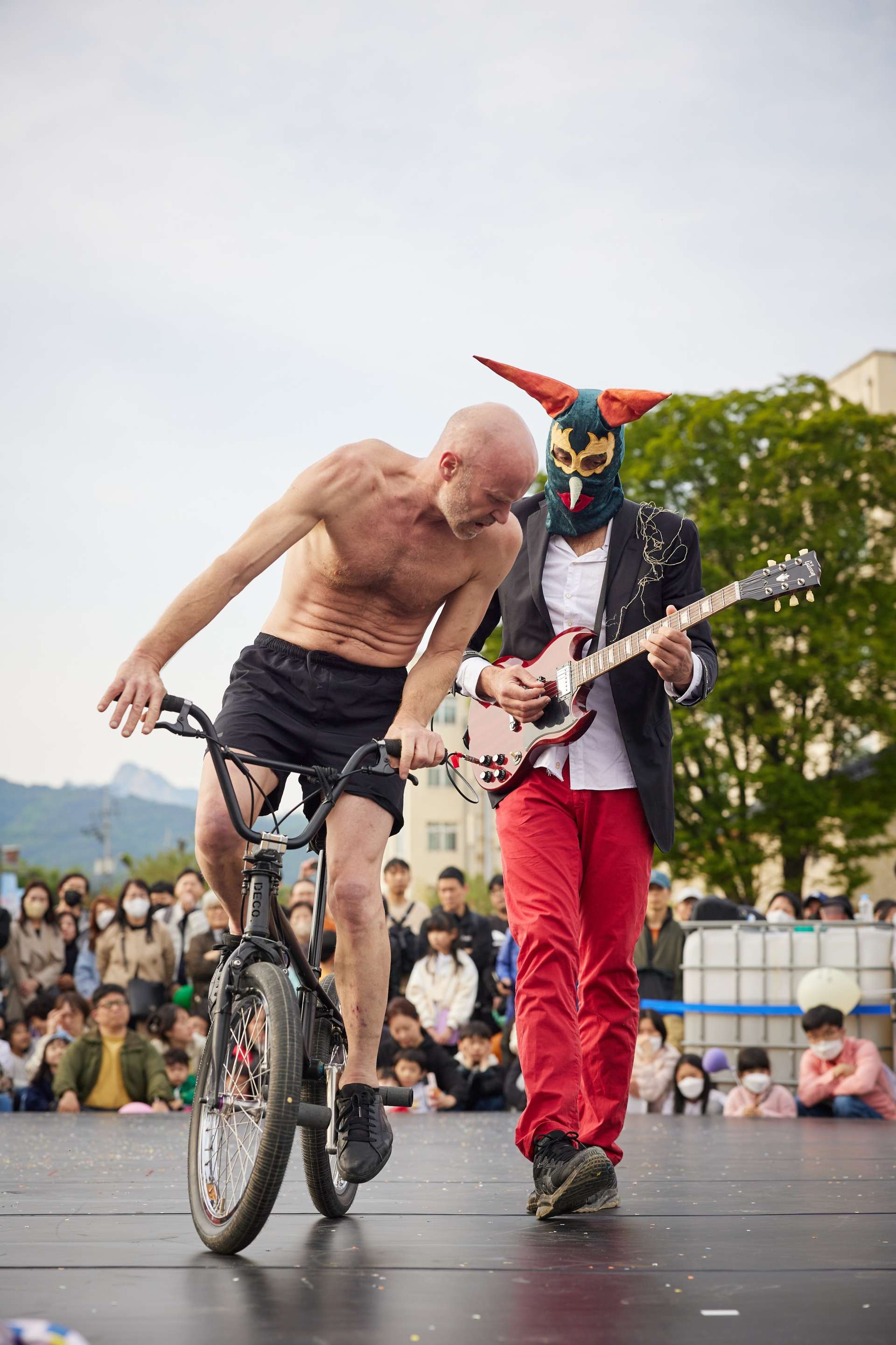 Un homme torse nu sur un vélo BMX regarde un guitariste qui le suite