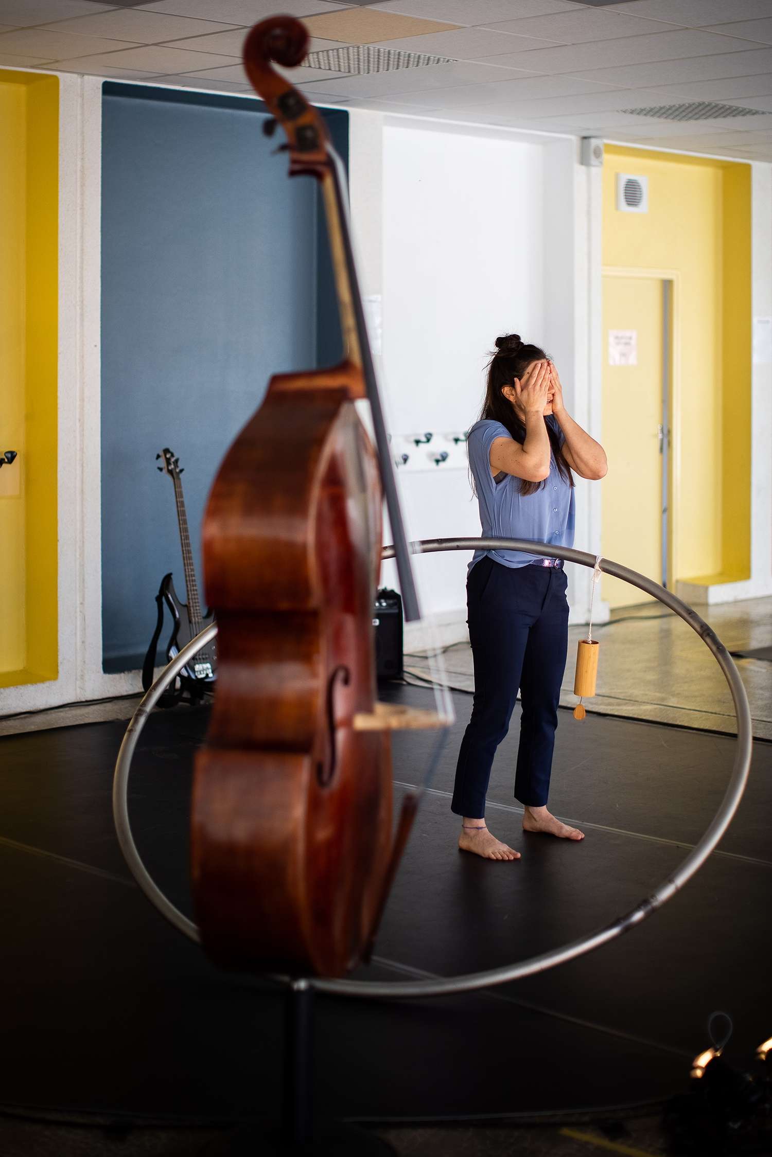 l'artiste se cache les yeux en arrière-plan, devant se trouve un violoncelle et un cerceau