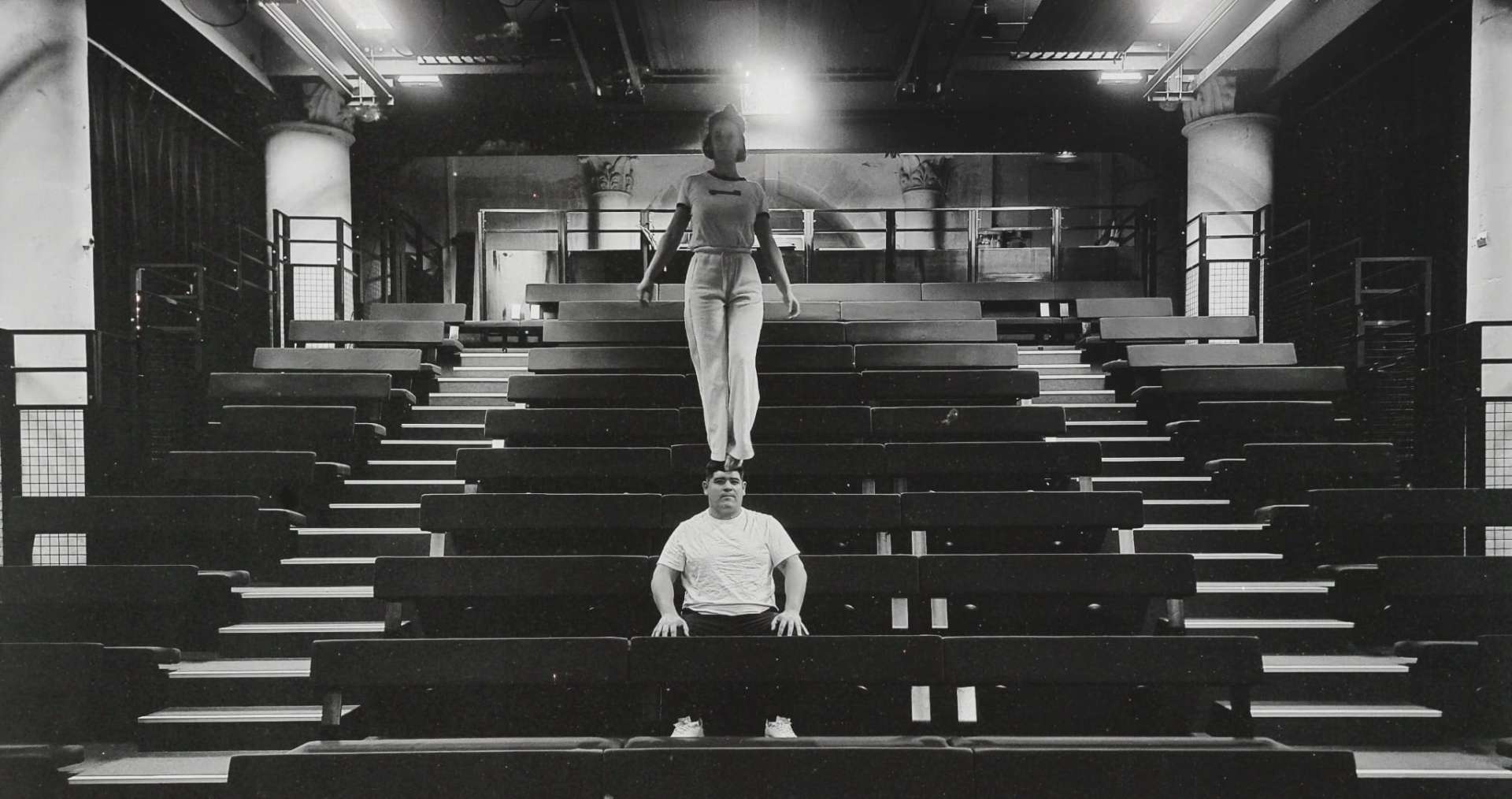 Une acrobate est debout sur la tête de son partenaire. Lui est assis dans les gradins.